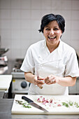 Woman chef peeling garlic with a knife and smiling\n