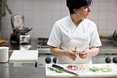 Woman chef peeling garlic with a knife looking to one side\n