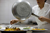 Köchin hält Bratpfanne und bereitet Nudeln mit Meeresfrüchten für den Service vor
