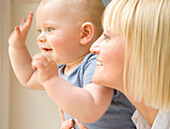 Close up of a baby waving his arms with his mother holding him\n