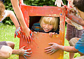 Junger blonder Junge in einem Pappkarton gefangen beim Spielen mit Freunden
