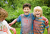 Young boys covered in watercolor paint laughing in a garden\n