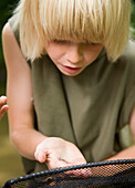 Young boy holding a fishing net inspecting a tadpole on his hand\n