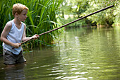 Junge angelt in einem Fluss mit den Beinen im Wasser