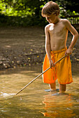 Junger Junge beim Fischen im Fluss mit Fischernetz