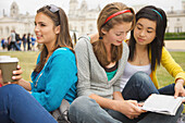 Mädchen im Teenageralter sitzen vor der Londoner Horse Guards Parade, trinken Kaffee und lesen ein Buch