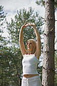 Junge Frau macht Yoga im Wald stehend in der Haltung der erhobenen Hände