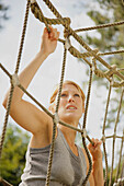 Young woman at obstacle course climbing a cargo net\n