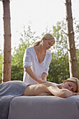 Female massage therapist massaging woman back in a forest\n