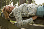 Young woman lying on a wooden beam smiling\n