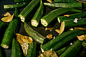 Close up vibrant green okra and leaves cooking in pan with oil and salt\n