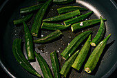 Vibrant green okra cooking in oil and salt in frying pan\n