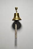 Brass bell with rope pull hanging on wall\n
