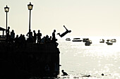Silhouetted teenagers dive into the sea from the town pier, Stone Town, Zanzibar island, Tanzania, East Africa, Africa\n