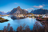 Abenddämmerung über dem majestätischen Berg Olstind mit Blick auf den ikonischen Hafen des Fischerdorfes Reine, Lofoten Inseln, Nordland, Norwegen, Skandinavien, Europa