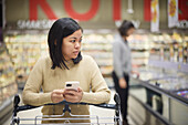 Frau beim Einkaufen im Supermarkt und mit Handy in der Hand