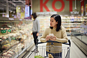 Frau beim Einkaufen im Supermarkt und mit Handy in der Hand