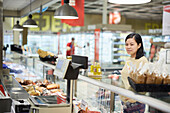 Kundin steht vor der Feinkosttheke im Supermarkt und prüft Produkte