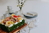 Schwedischer Sandwichkuchen mit Krabben, Käse, Schinken und Eiern auf Holzbrett am Tisch