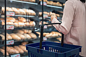 Woman with shopping basket in bakery section of supermarket\n