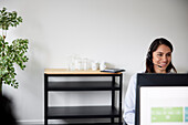 Smiling mid adult businesswoman using headset in office in front of computer screen\n