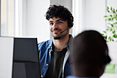 Junger Mann benutzt ein Headset, während er im Büro sitzt