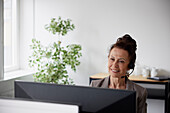 Smiling mature businesswoman using headset in office in front of computer screen\n