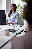 Lächelnde mittlere erwachsene Geschäftsfrau, die ein Headset im Büro vor einem Computerbildschirm benutzt