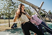 Sisters having fun swinging on swing on playground\n