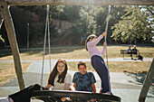 Siblings having fun swinging on swing on playground\n
