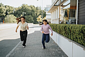 Happy sisters racing down sidewalk\n