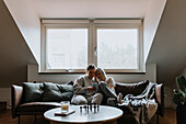 Weibliches Paar sitzt zusammen auf dem Sofa und schaut aufs Handy