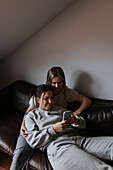 Weibliches Paar liegt zusammen auf dem Sofa und schaut auf das Handy