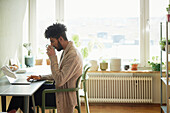 Mann mit Laptop am Tisch beim Kaffeetrinken