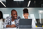 Lächelnde Mitarbeiter, die bei einem Geschäftstreffen sitzen und ein digitales Tablet benutzen