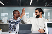 Lächelnde Mitarbeiter sitzen bei einem Geschäftstreffen und geben sich gegenseitig ein High-Five