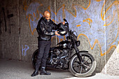 Mature biker in leather clothes standing next to motorcycle\n