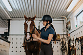 Frau im Stall bereitet Pferd zum Reiten vor