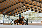 View of female horse rider using indoor riding paddock\n