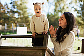 Mother looking at daughter playing at playground\n