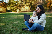 Mutter und Tochter sitzen im Herbstpark und benutzen ein Tablet