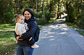 Smiling woman carry daughter and looking at camera\n