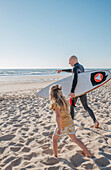 Blondes Mädchen mit Vater auf dem Surfbrett am Strand
