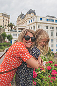 Cheerful mother and daughter posing in front of historical building\n