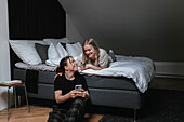 Homosexual female couple sitting on bed and looking at cell phone\n