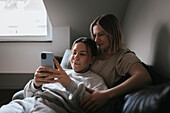 Homosexual couple sitting on sofa and using cell phone\n