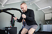 Man exercising with ropes in gym\n