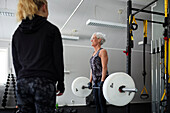 Mid adult woman looking at senior woman lifting weights\n