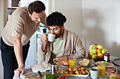 Happy gay couple eating breakfast at home\n