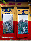 Humorous painted restroom doors at a cave tubing tour business in the Cayo District of Belize.\n